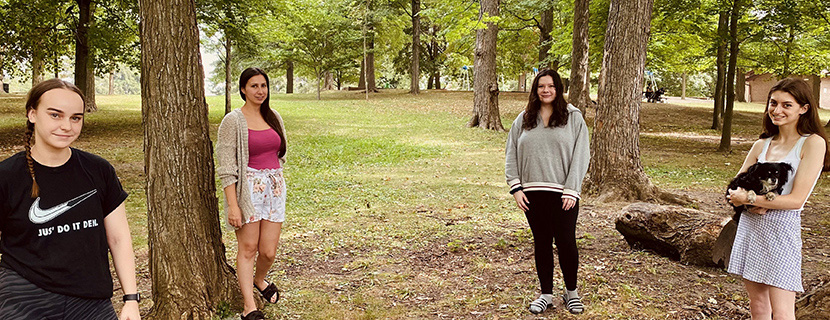Four students standing in front of trees