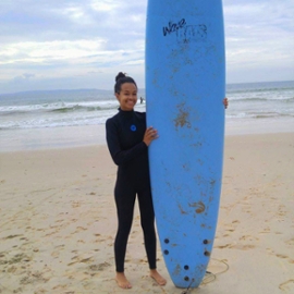 Eliana Rose on the beach with a surfboard