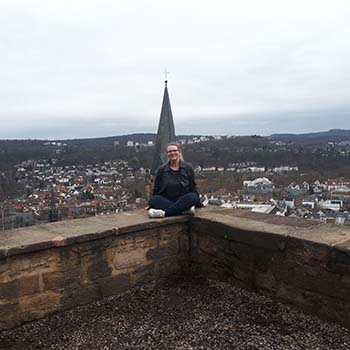 Spotlight story image pertaining to Student Morgan Lauzon sitting on a brick wall with a city skyline behind her