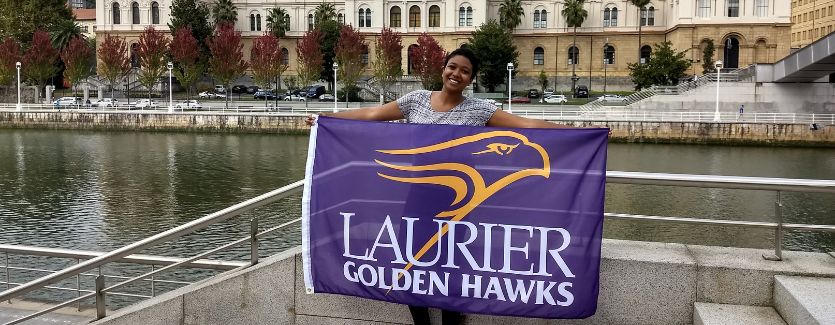 A student studying abroad holding a Golden Hawks flag.