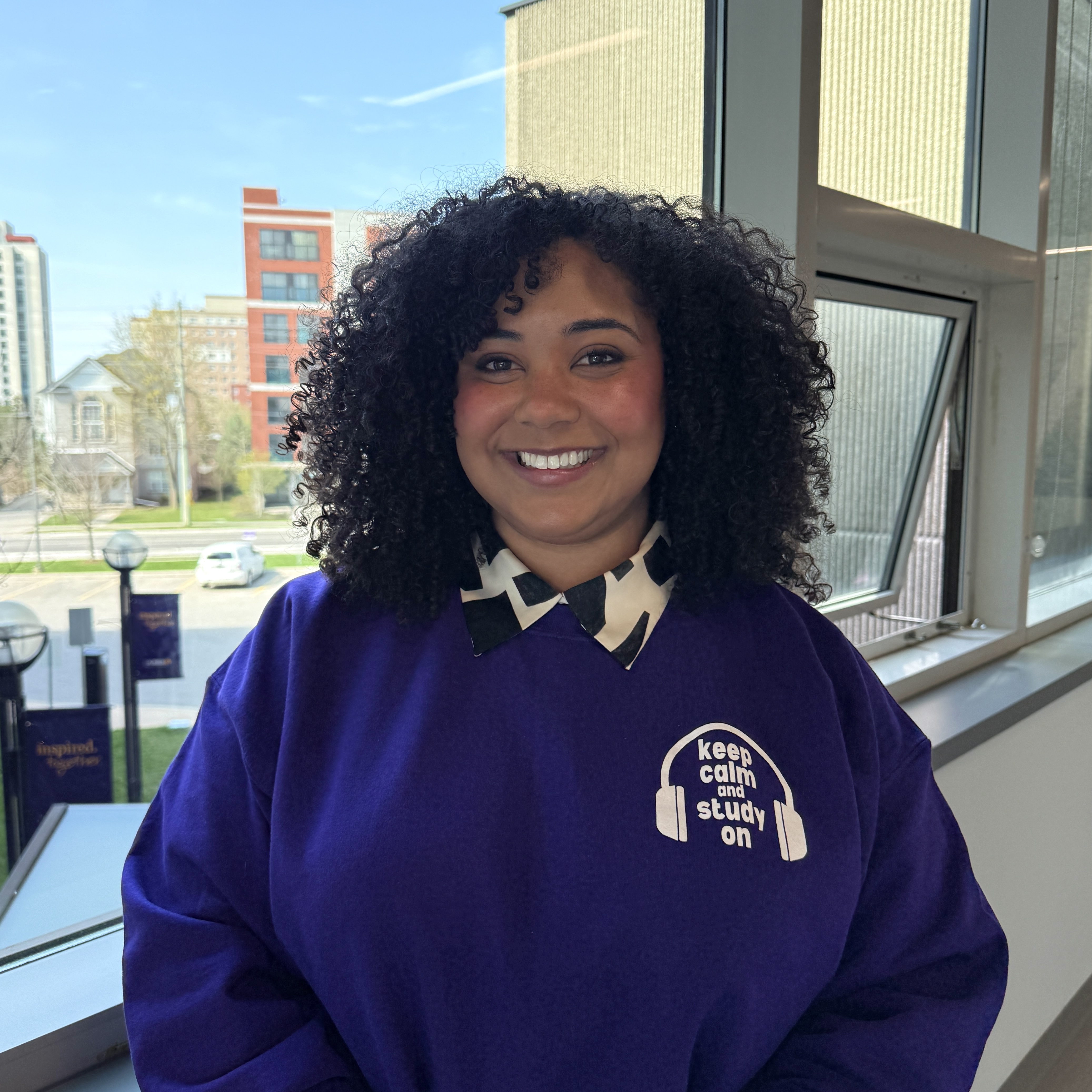 woman smiling with curly black hair, in a purple sweater