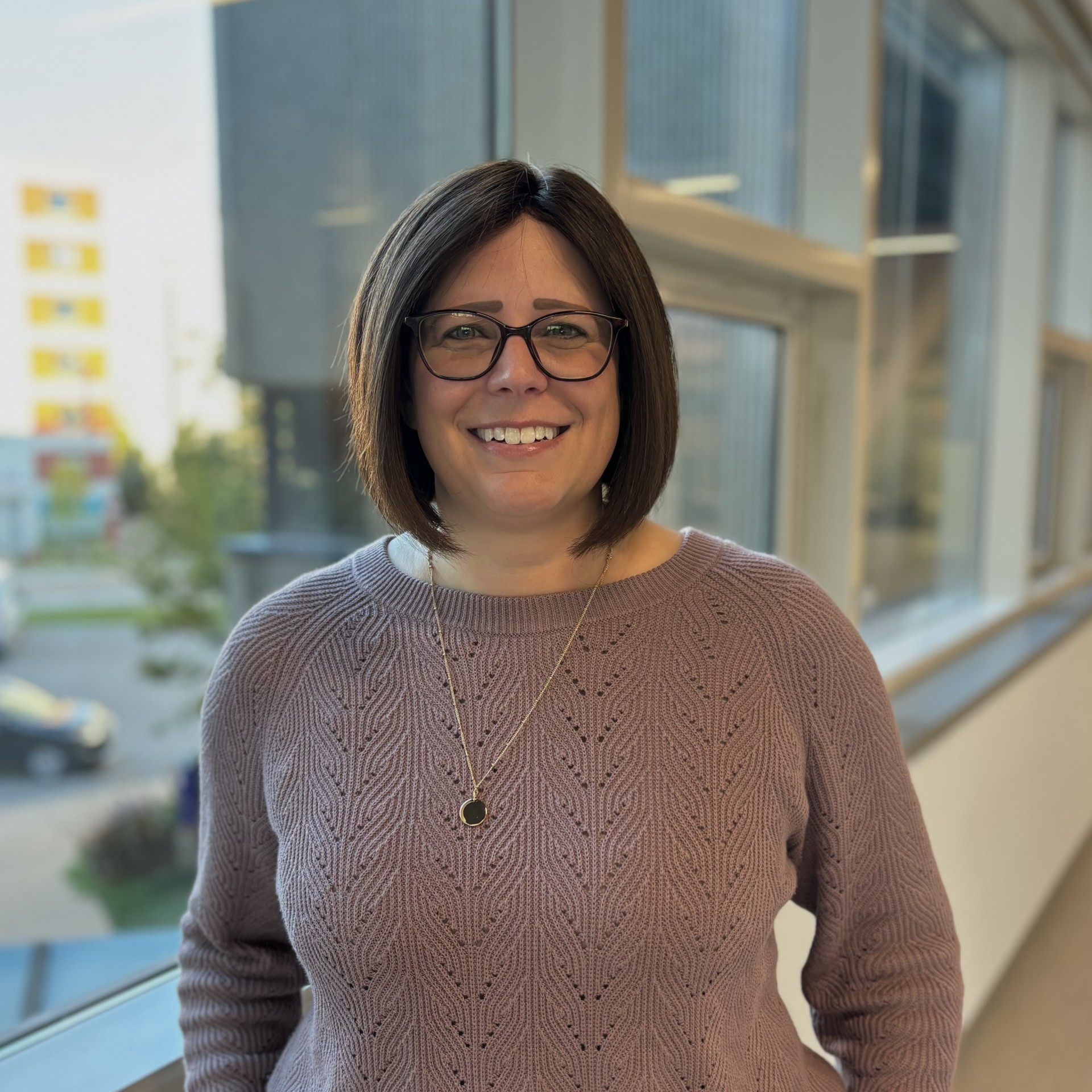 women with short brown hair smiling with brown glasses wearing a light purple knitted sweater