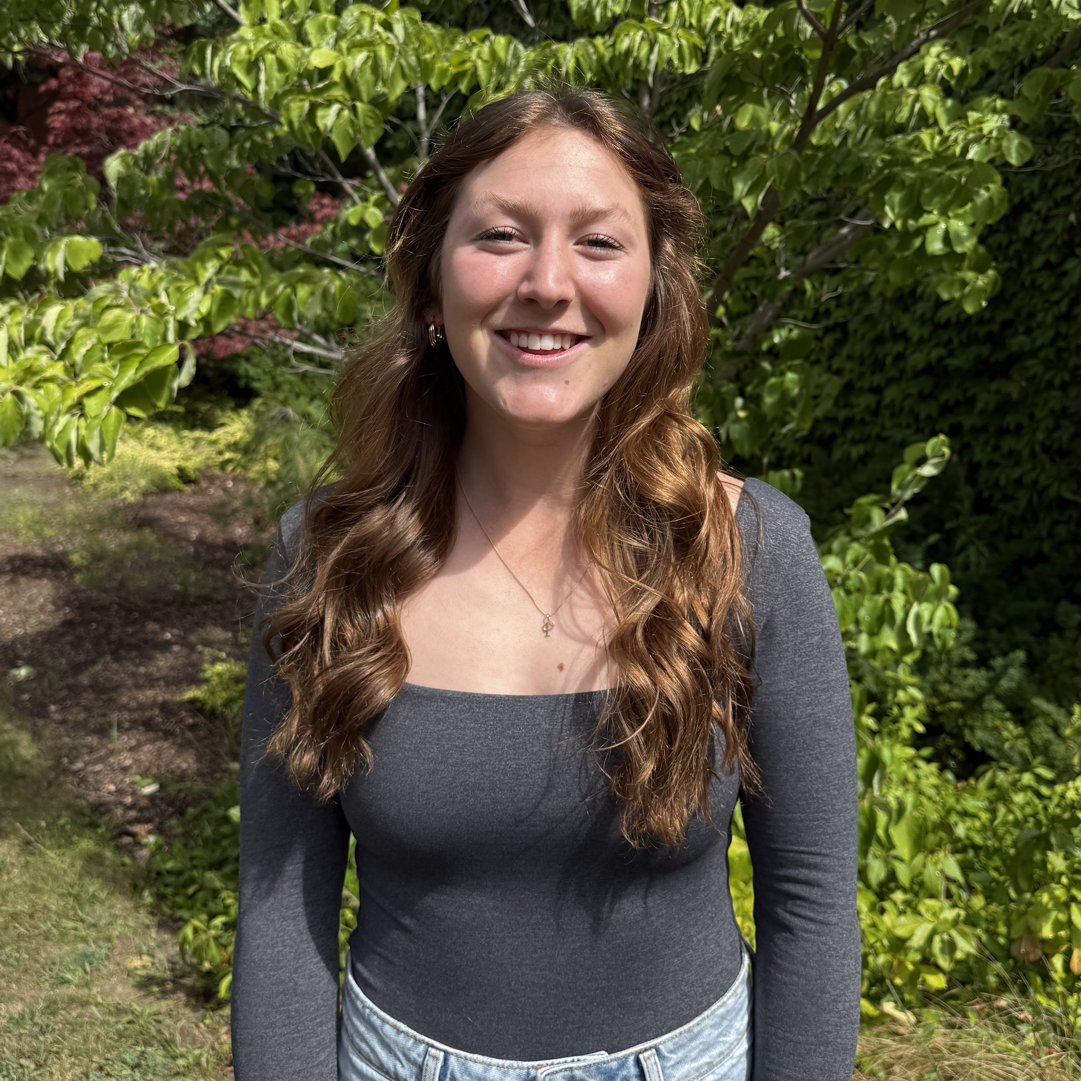 women with blond curly hair smiling in front of green trees