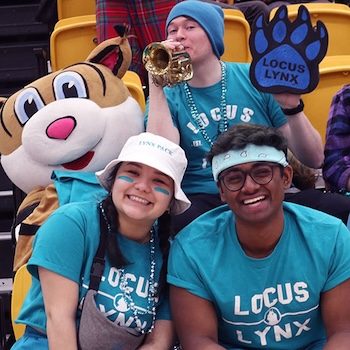 Students wearing LOCUS shirts sitting in stands with a lynx plushie