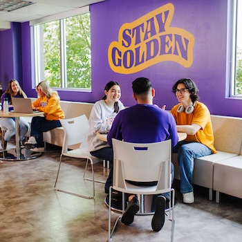 Students sitting at tables studying with Stay Golden letting on a wall in the background