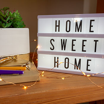 Home Sweet Home sign with pens and lights on desk