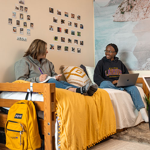Two students sitting on bed.