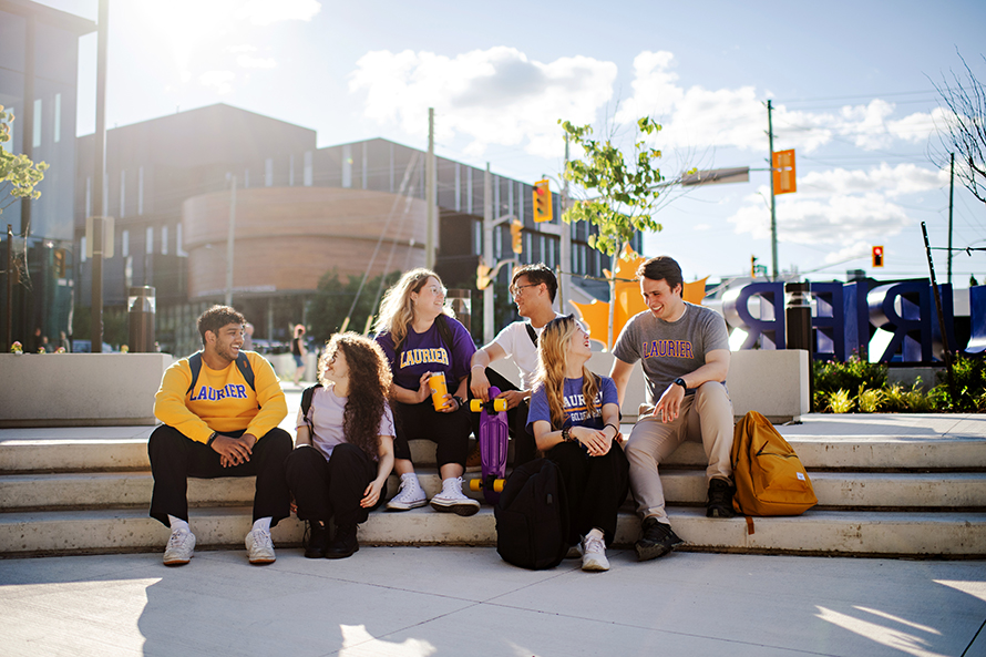 Students sitting outside casually in front of Lazaridis Hall