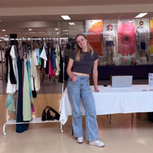Student posing next to clothing rack