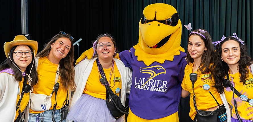 Five students posing with Midas the Goldenhawk mascot