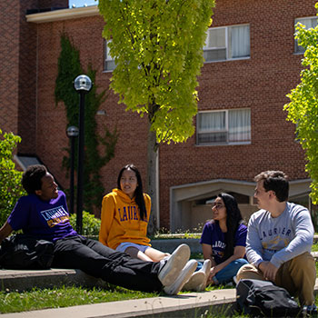 four students chatting and sitting on grass