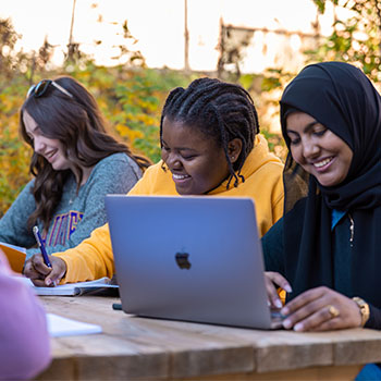 Students writing notes on a laptop and in a notebook