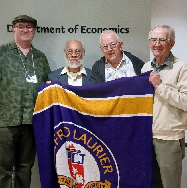 Laurier Economics Alumni Peter Friedmann, Terence Yhip and Alan Macnaughton, with former Chair of Economics Alastair Robertson, outside the Economics Department offices in Lazaridis Hall.