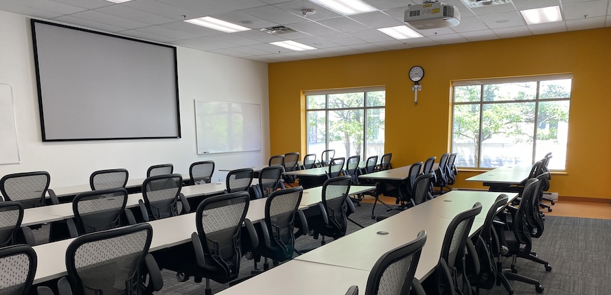 Inside a classroom with rows of desks facing a projector screen and a projector hanging from the ceiling