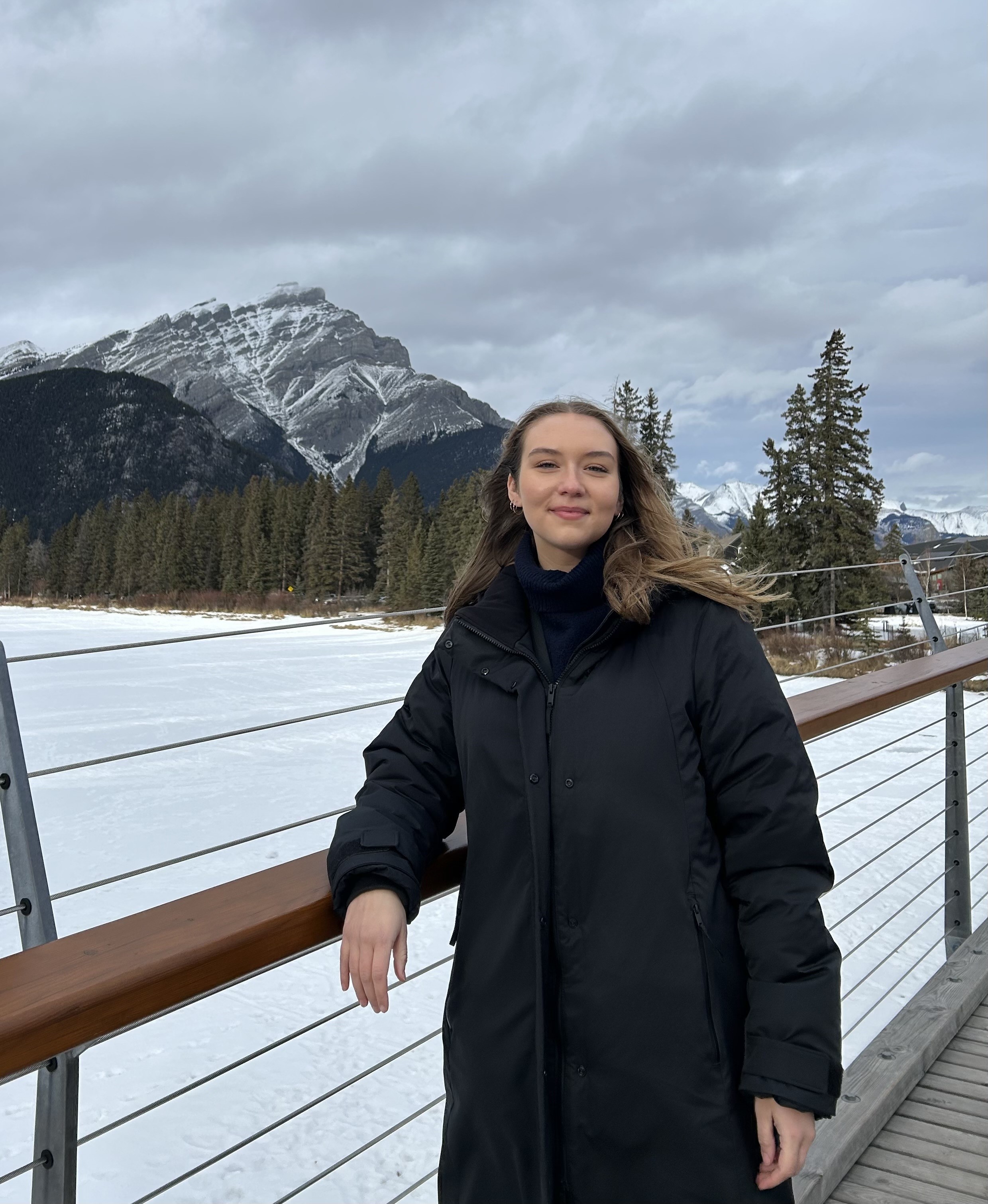 girls leaning on a railing, smiling with a frozen lake and mountains behind her