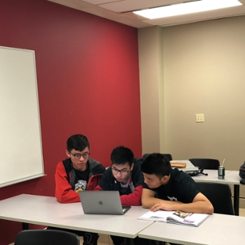 Three students sitting at a desk looking at a computer