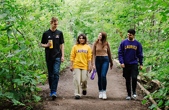 Four students walking along a path in the woods.