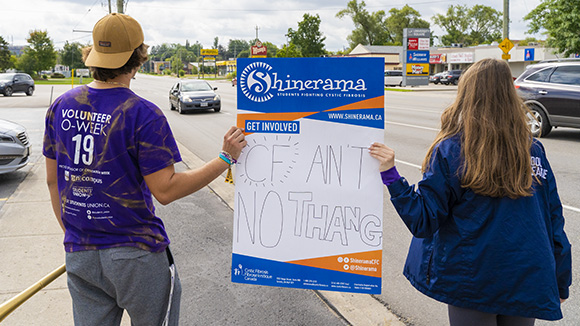 Students holding a Shinerama banner that says 'CF ain't no thang' on the side of the road