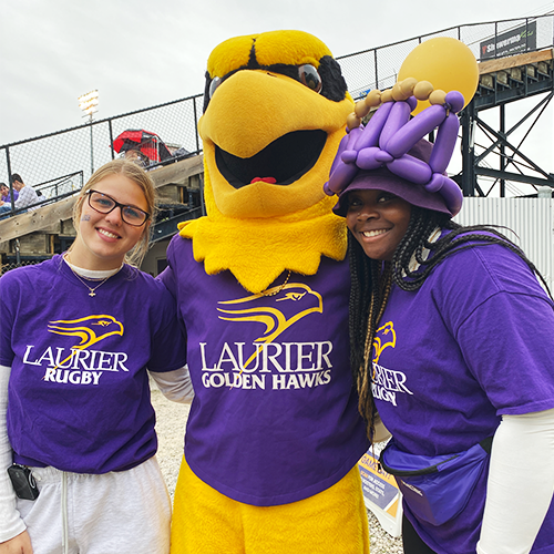 Golden Hawk mascot with two students wearing rugby shirts.