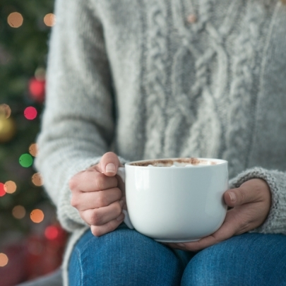 person holding mug in front of Christmas tree